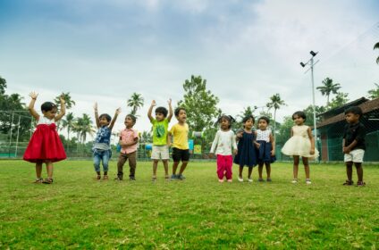 Children playing outdoors at The Backyard Academy preschool in Kakkanad, enjoying group activity on a green lawn.