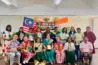 Group photo from an international learning and collaboration event featuring educators and participants from different countries, standing and seated on a stage with Malaysian and Indian flags in the background, holding awards and souvenirs in recognition of cross-cultural educational exchange.