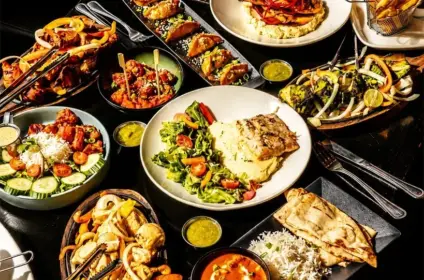 Bar and grill restaurant spread featuring burgers, grilled meats, seafood, salads, fries, and assorted dishes on a table