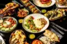 Bar and grill restaurant spread featuring burgers, grilled meats, seafood, salads, fries, and assorted dishes on a table